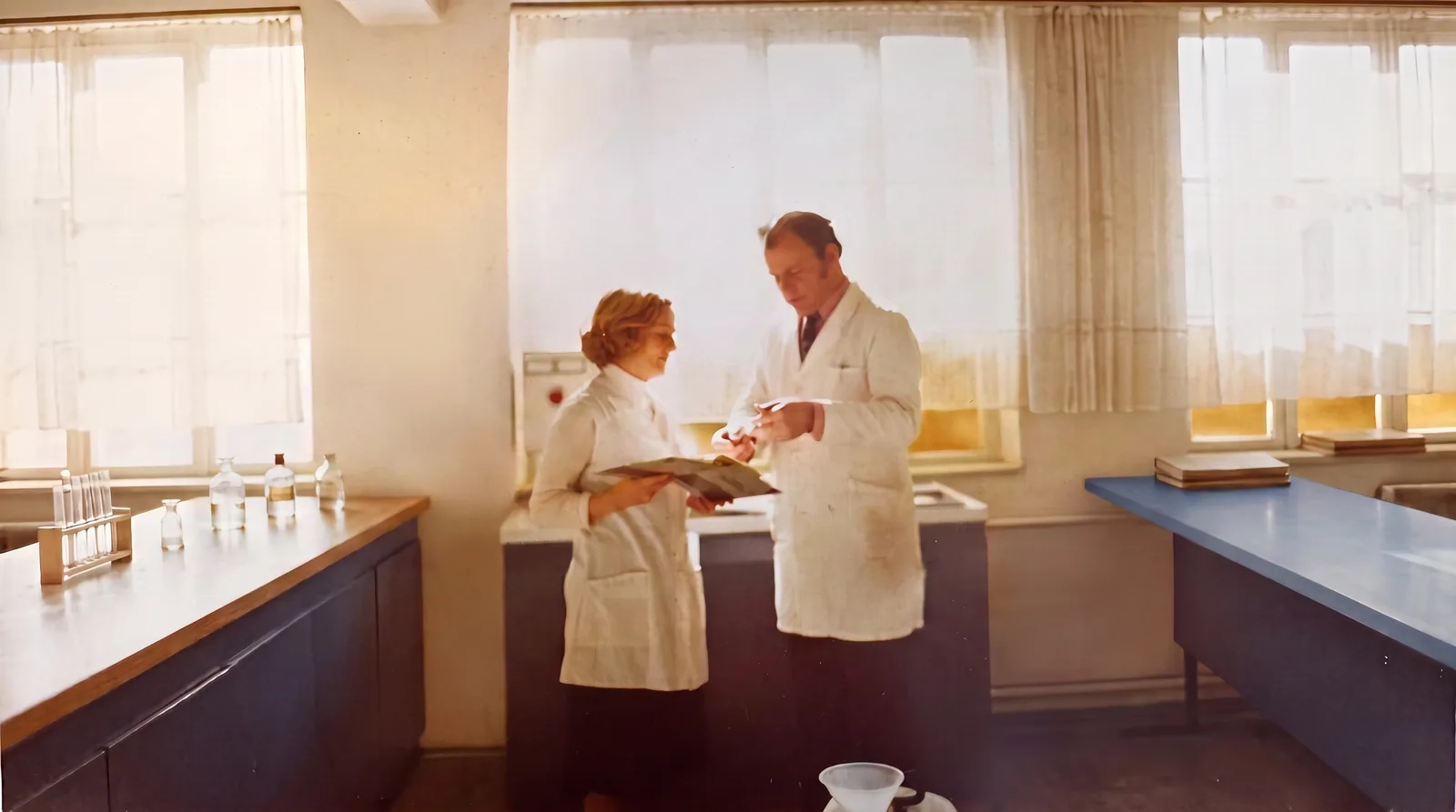 Historisches Foto aus den Anfangsjahren: Laborantin und Mitarbeiter im weißen Kittel besprechen Unterlagen